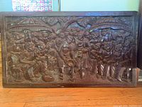 Front view of entire carved wood relief panel showing figures, umbrellas, and tree