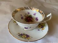 Teacup on saucer showing floral pattern, gold trim, handle style