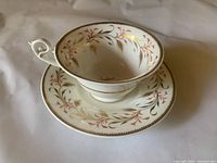 Teacup and saucer showing wheat and red leaf motif, gilt rims and handle