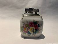 Front view of porcelain table lighter showing floral design and metal mechanism