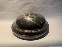 Side view of silver-plated oval domed meat cover showing finial and gadroon edge