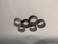 Six silver-tone cylindrical metal napkin rings laid flat on white background