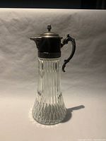 Full view of glass water jug showing glass body, pewter lid and handle