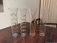 Front view of four clear champagne flutes showing unique gold accent patterns