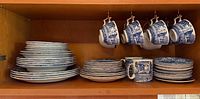 Cabinet shelf showing stacked plates, bowls, hanging teacups