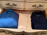 Drawer view showing blue turtleneck, cream cardigan, navy sweater folded