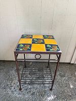Full view of metal side table showing tile top and lower slatted shelf