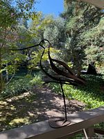 Full view of iron heron bird sculpture on railing with garden background