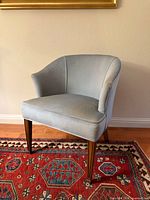 Front angle of light blue accent chair showing upholstery, curved back and wooden legs