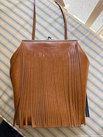 Front view showing brown leather, full fringe, metal frame, strap