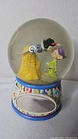 Front view of snow globe showing Snow White kissing Dopey and ornate base
