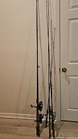 Three fishing rod and reel combos standing against wall