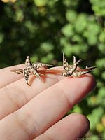 Brooch on fingertip showing two seed pearl swallows and bar