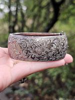 Wide sterling silver bracelet side view in hand displaying etched design