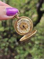 Pocket watch held with front cover open showing dial