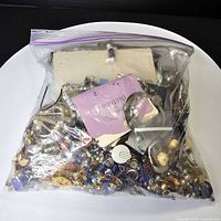 Full Ziploc bag filled with assorted jewelry parts and beads on white surface