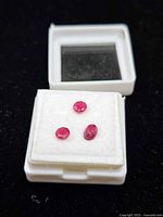 Three loose ruby gemstones in open plastic display box