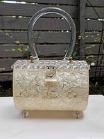 Front view of lucite barrel purse showing body, lid, handle, latch, and feet