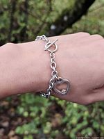 Bracelet worn on wrist showing scale, rolo links, toggle clasp, heart charm