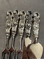 Five utensils showing grapevine handles and utensil ends