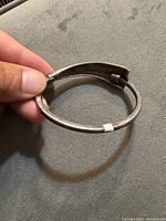 Hand holding sterling silver hinged bracelet showing overall shape and patina