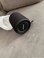 Speaker left side showing mesh exterior and logo on passive radiator