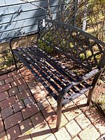 Full view of black metal bench on patio showing lattice back and slatted seat