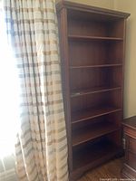 Full view of tall wooden bookcase next to curtain