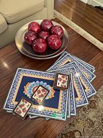 Bowl with ceramic pomegranates on table beside stacked placemats and two coasters