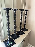 Four black metal candlesticks on shelf