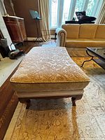 Full view of bench showing upholstered top, wooden legs, surrounding furniture for scale