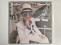 Front cover showing Elton John seated in white suit and hat