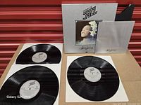 Three vinyl records, booklet and box displayed