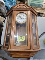 Front view of Bulova wall clock showing full wooden case, glass panels, dial, pendulum