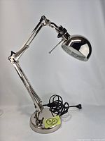 Full view of chrome articulated desk lamp showing base, arm, shade, cord