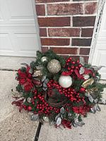Full view of decorated Christmas wreath leaning against brick and garage door