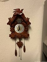 Full view of carved wooden quartz cuckoo wall clock with weights and pendulum