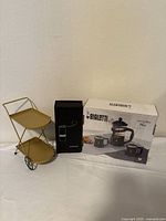 Overall lot showing boxed Bialetti set, black grinder box, gold two-tier cart