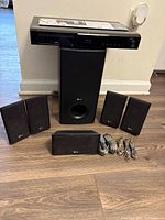 Front view of entire LG home theater system showing receiver on top of subwoofer, four satellite speakers, center speaker and wiring