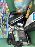 Bin containing bath bombs, hammer, travel mug, paint kit packaging and assorted electronics