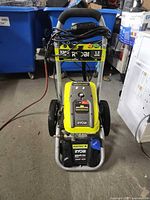 Front view of Ryobi electric pressure washer showing handle, rating label 2300 PSI 1.2 GPM, power cord wrapped on handle