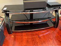 Front view of black tempered glass TV stand showing three shelves and chrome accents