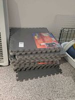 Stack of grey EVA interlocking floor mats, several sealed packs visible