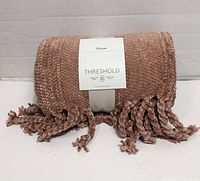 Rolled dusty rose chenille throw with paper band and fringe visible