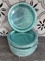 Stacked sealed packs of turquoise glitter paper plates