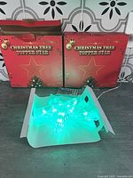 Two product boxes labelled Christmas Tree Topper Star behind one illuminated star and remote.
