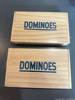 Two sealed wooden dominoes boxes, lids showing "DOMINOES" text