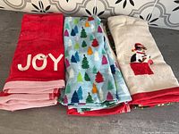 Three folded towel pairs showing JOY, tree print, dog graphic designs