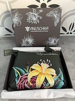 Pouch front in box with lid showing Anuschka branding