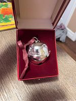 Bell in open red velvet-lined box showing ribbon and polished surface